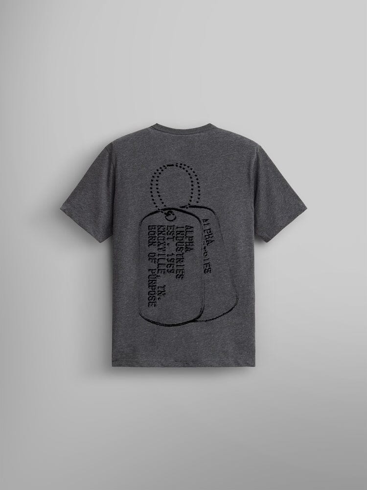 The Alpha Dog Tag Tee by Alpha Industries, is a gray T-shirt with a unisex design. It features a screen-printed graphic of dog tags on the back, accompanied by text, including the phrase "Born Of Purpose".