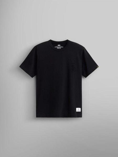 Alpha Dog Tag Tee by Alpha Industries, is a black short-sleeve t-shirt showcased on a plain gray background. It features a small screen print graphic emblem and label near the hemline.