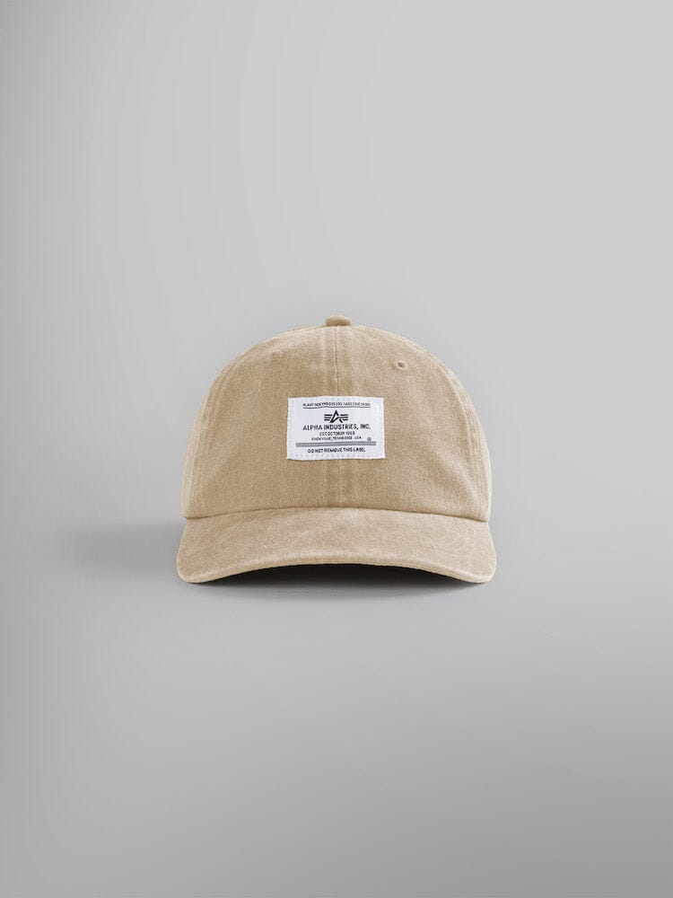 The Battlewash Cap by Alpha Industries, a vintage-inspired baseball cap in vintage khaki featuring a white rectangular patch with text and an Alpha logo on the front.