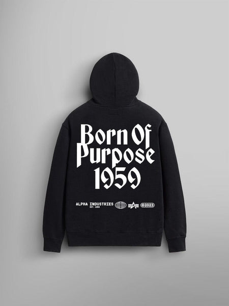 The Born Of Purpose Hoodie by Alpha Industries features a unisex design in black heavy cotton. It prominently displays "Born Of Purpose 1959" in bold white letters on the back and includes a handy kangaroo pocket along with logos for Alpha Industries beneath it.