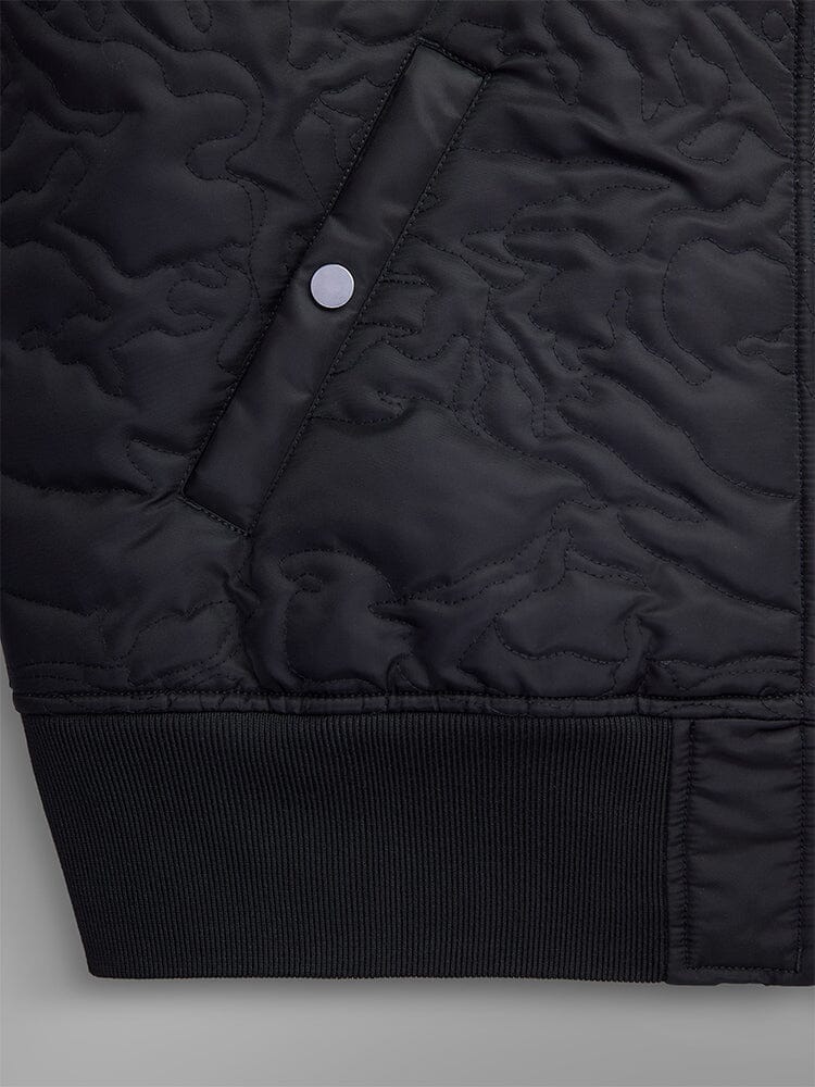 Detailed view of the Camo Quilted MA-1 Bomber Jacket by Alpha Industries, showcasing a black quilted pattern with a camouflage design, side pocket with a snap button closure, water-resistant material, and ribbed cuffs.