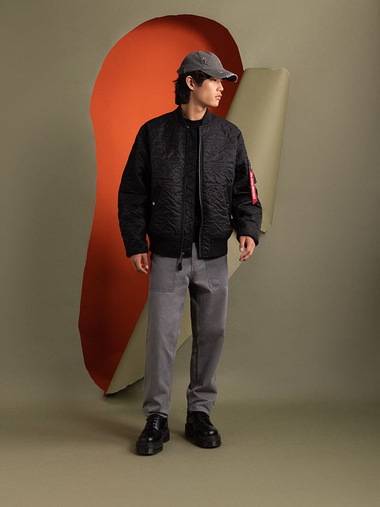 A person wearing the Alpha Industries Camo Quilted MA-1 Bomber Jacket in black.