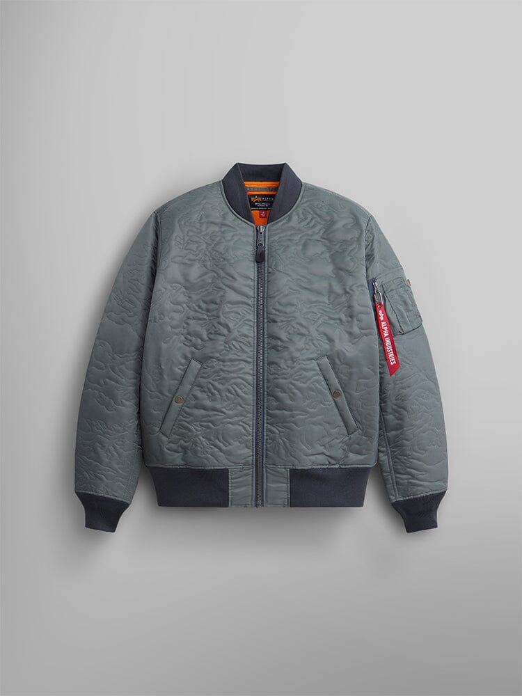 The Camo Quilted MA-1 Bomber Jacket in field gray by Alpha Industries, highlighted by its front zipper, side pockets, and signature MA-1 utility pocket. Ribbed cuffs, and a red tag attached to the sleeve provides an extra touch of flair.