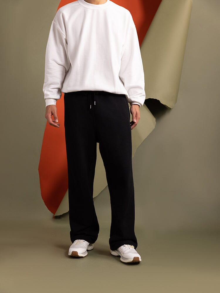 A person dressed in a white sweatshirt and stylish black Essential Sweatpants featuring an elastic waistband complements their outfit with white sneakers.