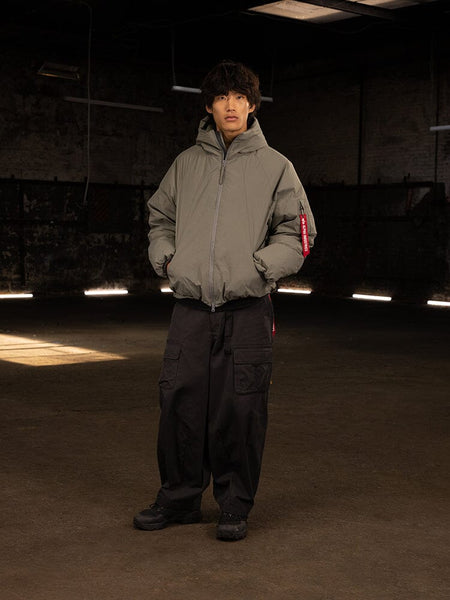 An individual stands wearing an Alpha Industries Insulated Hooded Parka with responsible down fill and black cargo pants, hands snugly tucked in pockets.