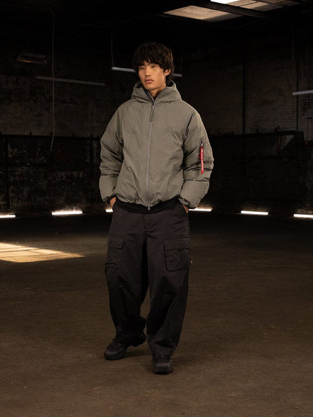 A person wearing an Insulated Hooded Parka by Alpha Industries, paired with black cargo pants, their attire hinting at the practicality of water-resistant materials.