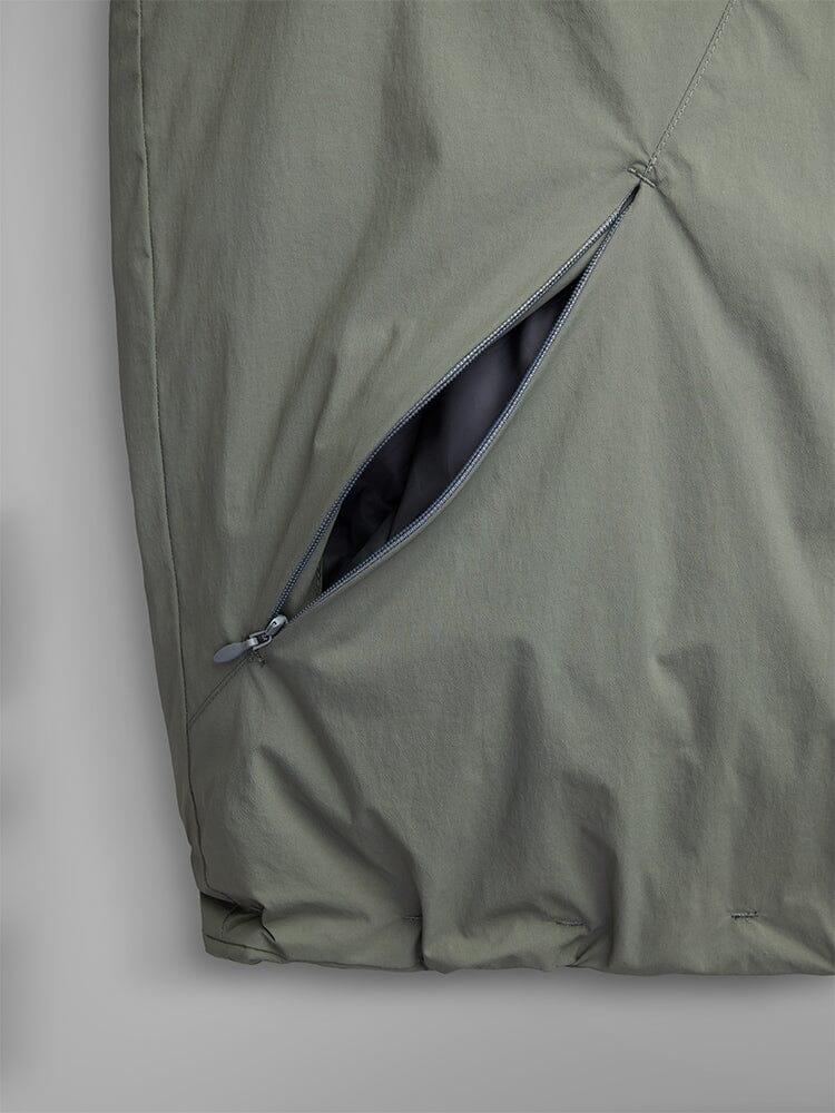 A close-up of the Insulated Hooded Parka by Alpha Industries reveals a green fabric with a partially open zipper pocket, providing a peek at the black lining inside. This parka perfectly combines style with functionality through its water-resistant material, making it an excellent choice for casual wear.