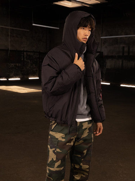 A person wearing the Alpha Industries Insulated Hooded Parka and camouflage pants stands indoors.