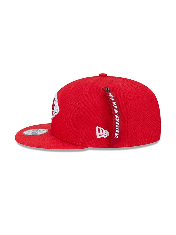 The Kansas City Chiefs x Alpha x New Era 950 Cap, featuring Alpha Industries branding and a small tag, showcases a classic snapback design that expertly combines style with a contemporary touch.