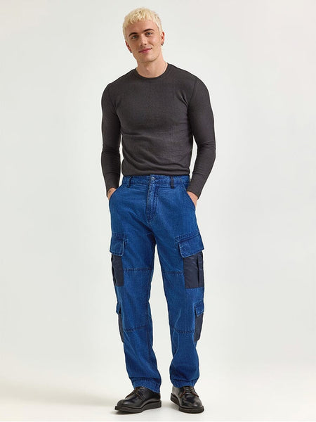 A person with short blonde hair is wearing a dark long-sleeve shirt and the Alpha X Lee Acu Pant in Indigo by Alpha Industries, which features military design elements.