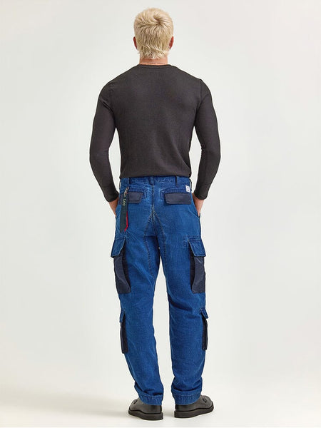 A person with short blond hair, dressed in a black long-sleeve shirt and the Alpha X Lee Acu Pant by Alpha Industries, known for its blue ripstop cotton fabric and military design pockets, paired with black shoes, is facing away from the camera.