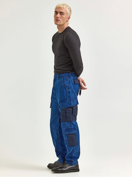 A person with short blonde hair, wearing a long-sleeve black shirt and the Alpha X Lee ACU Pant by Alpha Industries, crafted from sturdy ripstop cotton in blue.