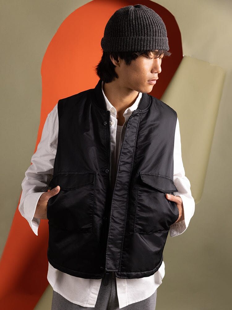 An individual wearing the Alpha Industries MA-1 Mod Vest in black, paired with a white shirt, gray beanie, and gray pants.