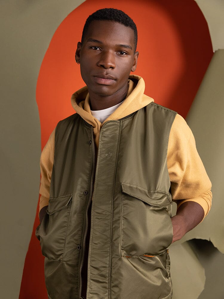 A person wearing the Alpha Industries MA-1 Mod Vest in OG-107 Green, known for its water-resistant properties.