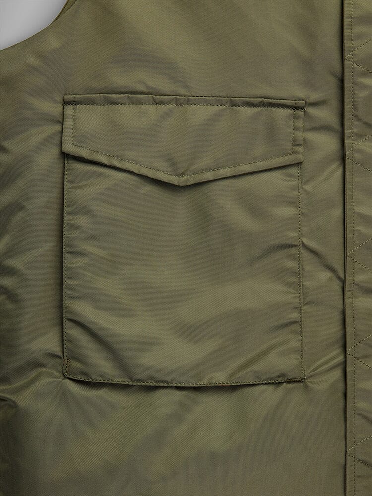 A close-up view of the olive green fabric on the MA-1 Mod Vest by Alpha Industries highlights a square patch pocket with a flap, accentuated by visible stitching along the seams.