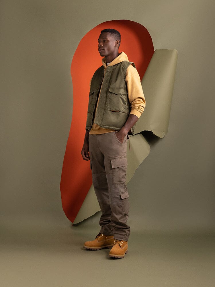 Side view of a person wearing the MA-1 Mod Vest by Alpha Industries. The water-resistant flight nylon vest with quilted lining is styled over a yellow hoodie.