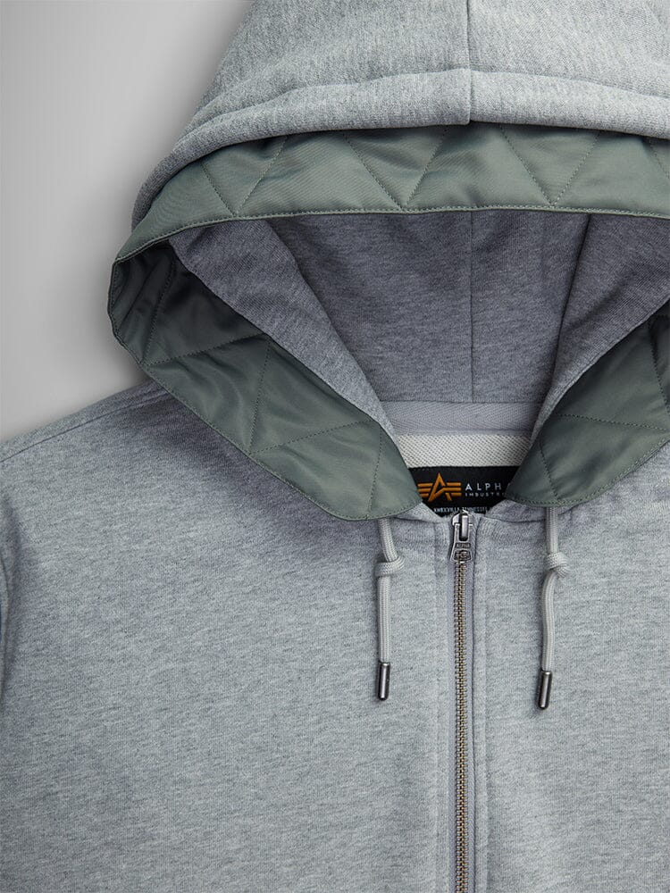 The MA-1 Zip Up Hoodie from Alpha Industries features a gray design with flight nylon sleeves, green quilted lining in the hood, and sleek drawstrings.