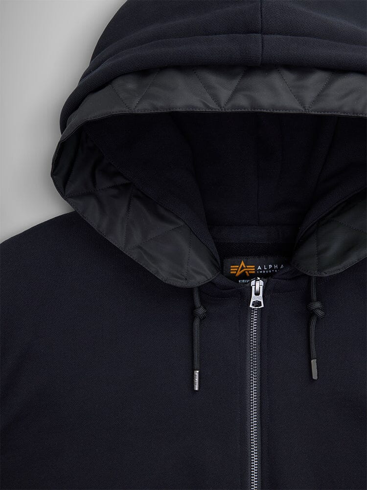 Close up of the Alpha Industries MA-1 Zip Up Hoodie features a black zip-up design with flight nylon sleeves, a quilted inner lining, silver zipper, and drawstrings.