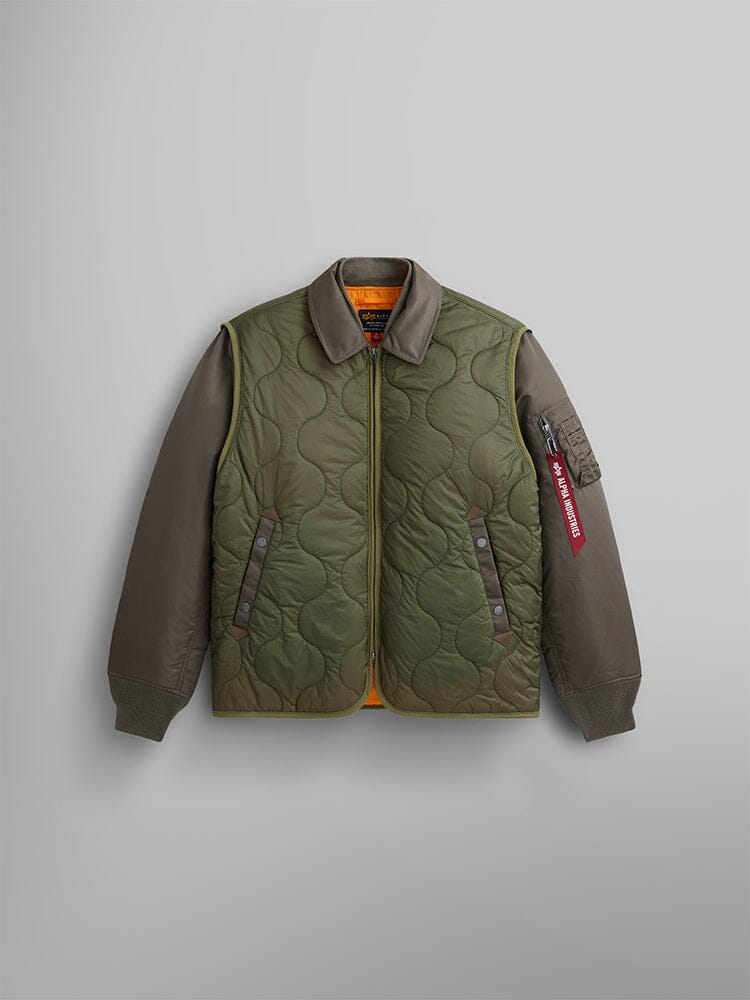 A coyote brown Mixed Media Quilted Utility Jacket by Alpha Industries, featuring a dark collar and sleeves, along with a red Remove Before Flight tag on the left sleeve.