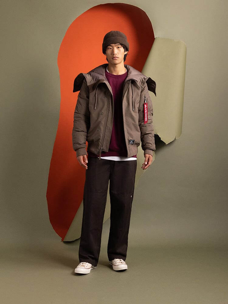 A person wearing the N-2B Altitude Parka in brown by Alpha Industries, paired with a maroon shirt and brown pants.