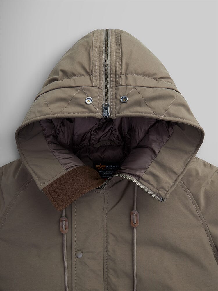 A close-up of the N-2B Altitude Parka by Alpha Industries displays its zippered front and brown hue. The water-resistant fabric features an adjustable split hood, which opens to reveal a darker inner lining with two drawstrings.