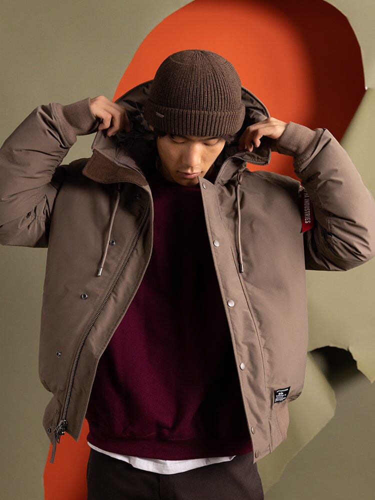 A person wearing an Alpha Industries N-2B Altitude Parka in brown and a matching brown knit hat.