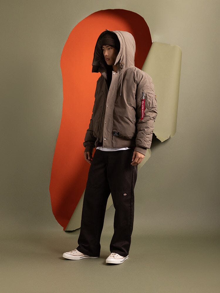 A person standing to the side wearing the hood up on the N-2B Altitude Parka in brown by Alpha Industries.