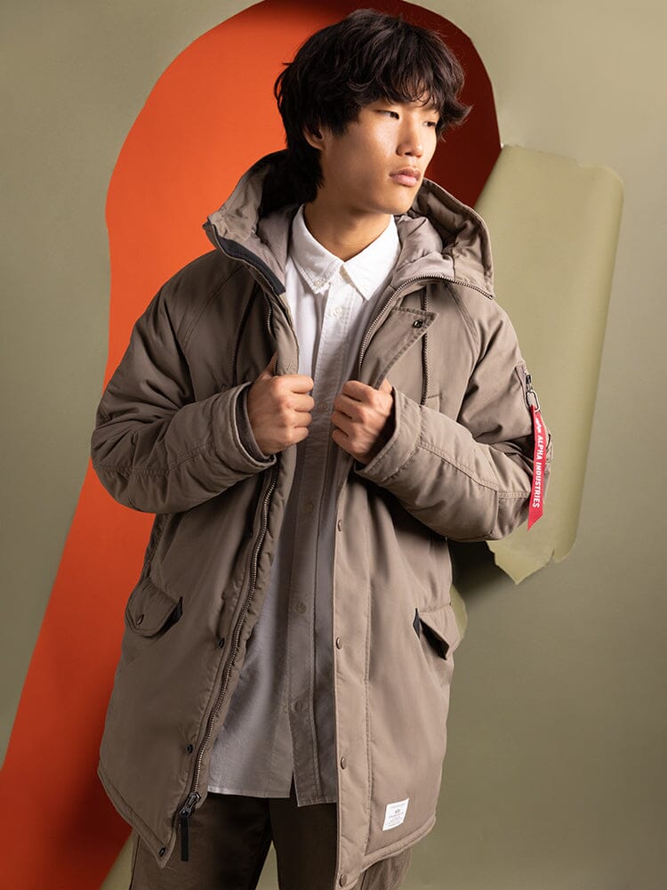 A person wearing an Alpha Industries N-3B Altitude Mod Parka in brown over a white shirt.