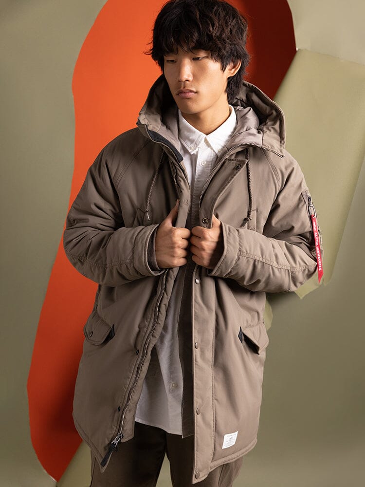 A person wearing the N-3B Altitude Mod Parka, a water-resistant brown hooded jacket by Alpha Industries.