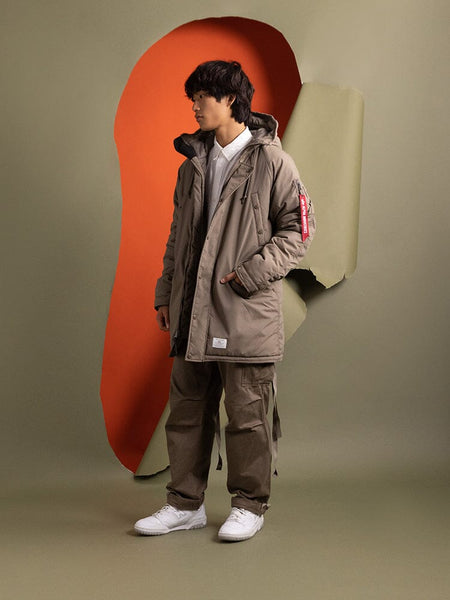 A person standing to the side wearing the N-3B Altitude Mod Parka in brown by Alpha Industries.