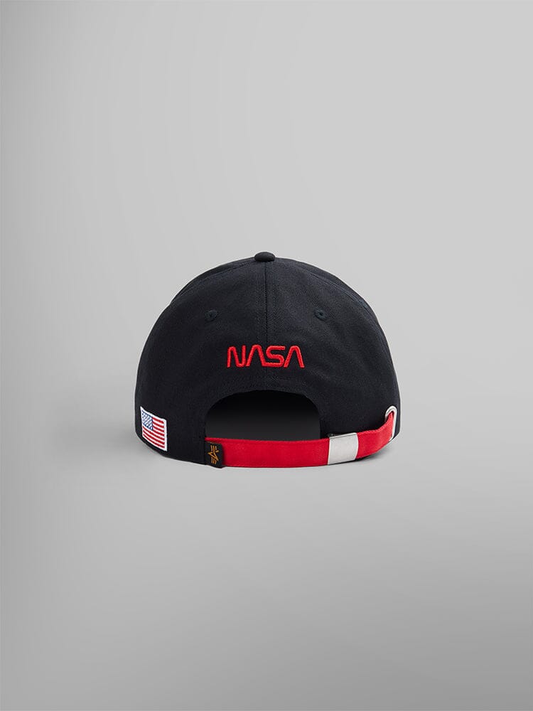 The NASA Worm Logo Cap by Alpha Industries is a black baseball cap featuring the iconic NASA worm logo in red on the back. It includes an American flag patch and a vibrant red and white adjustable strap.