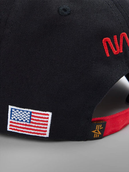 Close-up of the NASA Worm Logo Cap by Alpha Industries. This unisex black baseball cap features a red brim, an embroidered U.S. flag, red initials, and the iconic NASA worm logo on the side.