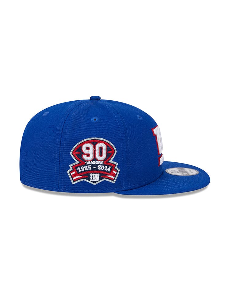 New York Giants x Alpha Industries x New Era 950 Cap, crafted by Alpha Industries, is a blue snapback cap adorned with a "90 seasons 1925-2014" patch on the side. It features striking red and white embroidery along with a bold team logo.