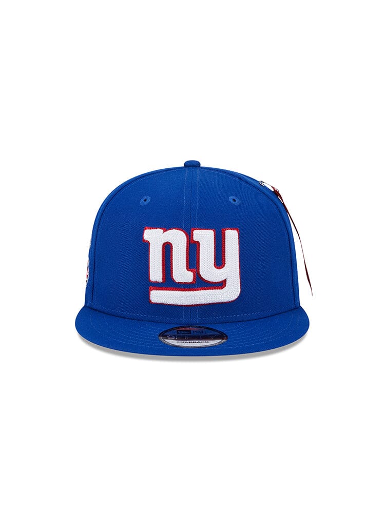 A blue snapback baseball cap boasting the classic white and red NY team logo on the front, crafted with Alpha Industries® quality, known as the New York Giants X Alpha X New Era 950 Cap.