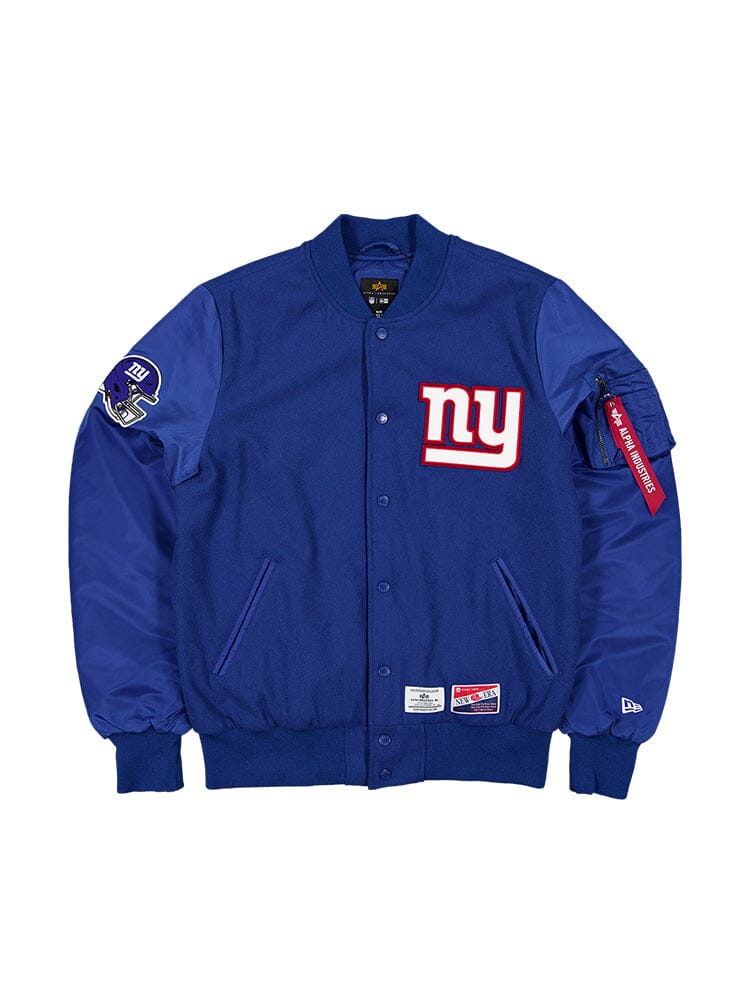 The New York Giants x Alpha x New Era MA-1 Bomber Jacket by Alpha Industries in Pacific Blue showcases the iconic NY logo on the front and features a G-Men patch on the sleeve along with an NFL team patch for the New York Giants. It integrates classic style elements, including a zipper pocket and red tag on the arm, reminiscent of an MA-1 Bomber Jacket.