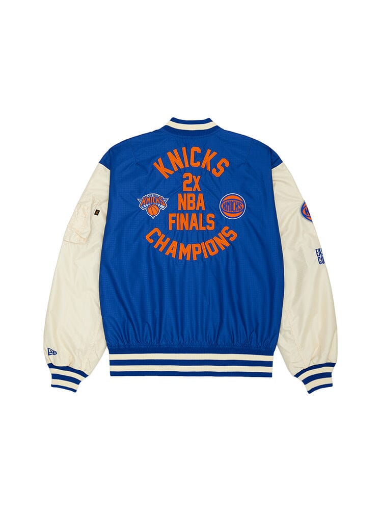 The New York Knicks x Alpha X New Era L-2B Bomber Jacket by Alpha Industries showcases the iconic Knicks blue and white palette, embellished with the phrase "2X NBA Finals Champions" and intricate team patches and logos on the back for a striking look.