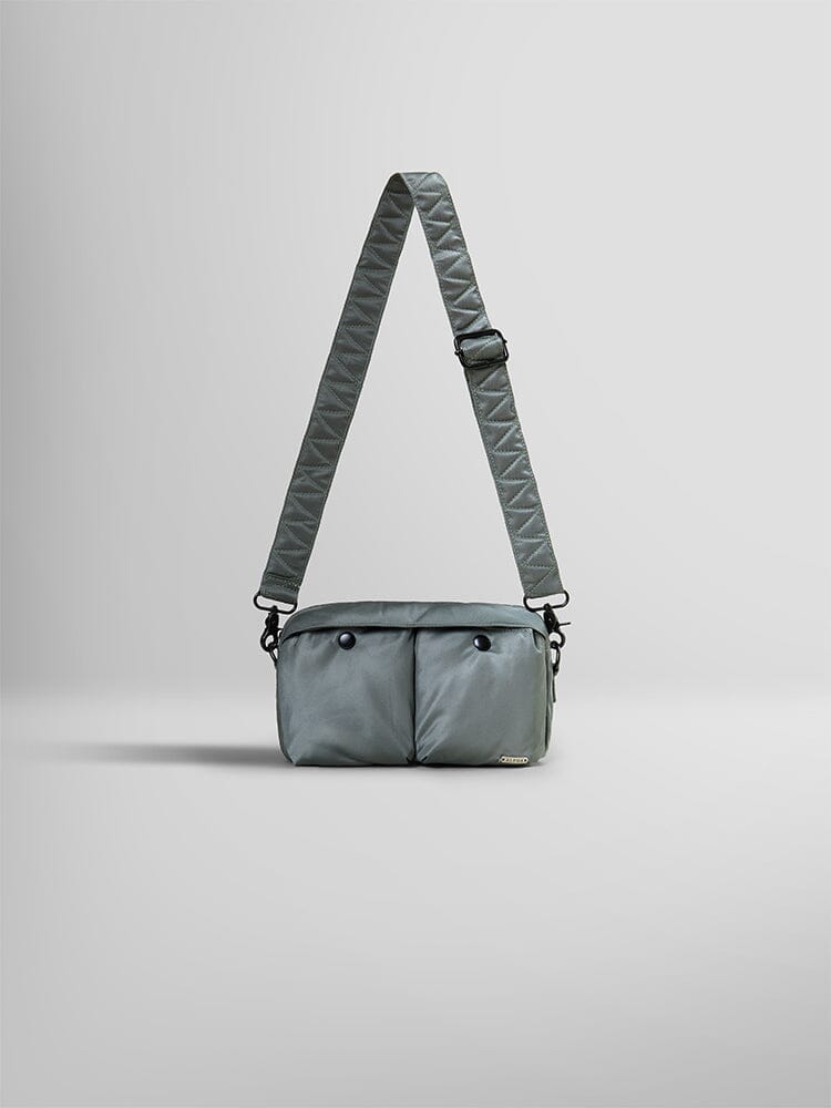 The Nylon Messenger Bag by Alpha Industries, in a sleek field gray hue, is crafted from durable nylon and features two front pockets along with an adjustable shoulder strap.