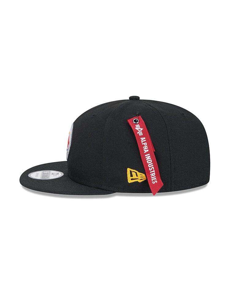 Pittsburgh Steelers x Alpha x New Era 950 Cap by Alpha Industries in black, featuring a red Alpha Industries tag, yellow logo embroidery on the side, and a sticker on the brim.