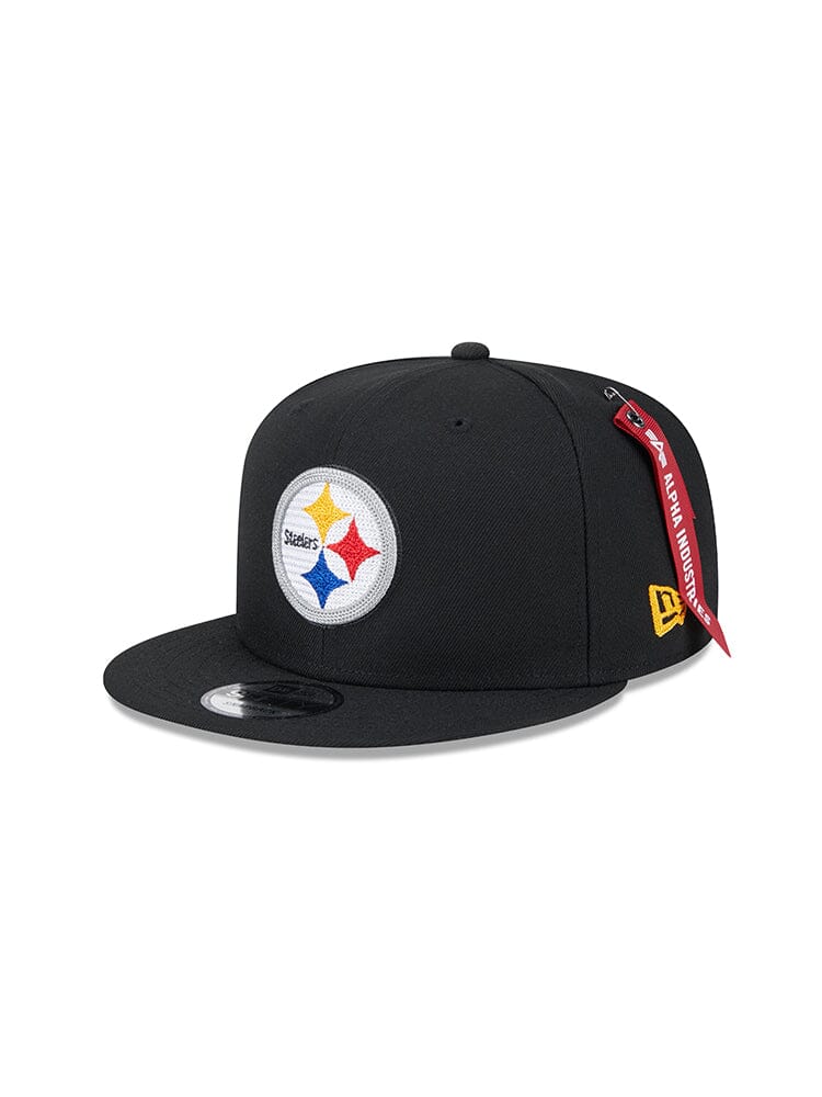 This Pittsburgh Steelers x Alpha x New Era 950 Cap in black features a circular team logo with three stars and "Steelers" at the center. It also boasts Alpha Industries' signature red tag for added unique style.