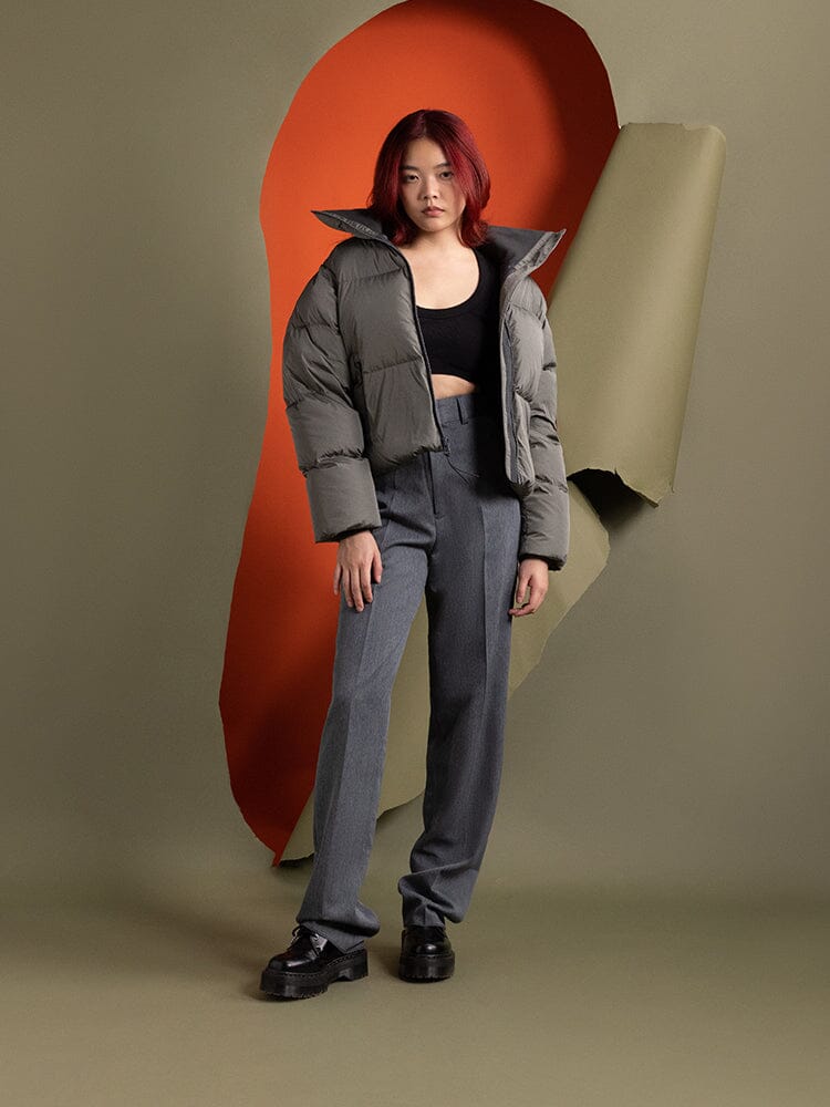 A person with red hair stands wearing the Sierra Short Puffer W by Alpha Industries, paired with a black top, gray pants, and black shoes.