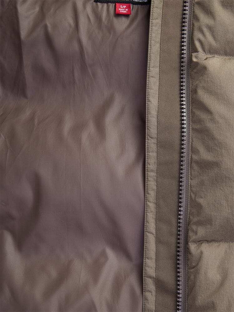 Close-up of an open brown Sierra Short Puffer W jacket by Alpha Industries, featuring a visible zipper and a red clothing tag at the top. The water-resistant fabric makes it ideal for chilly days.