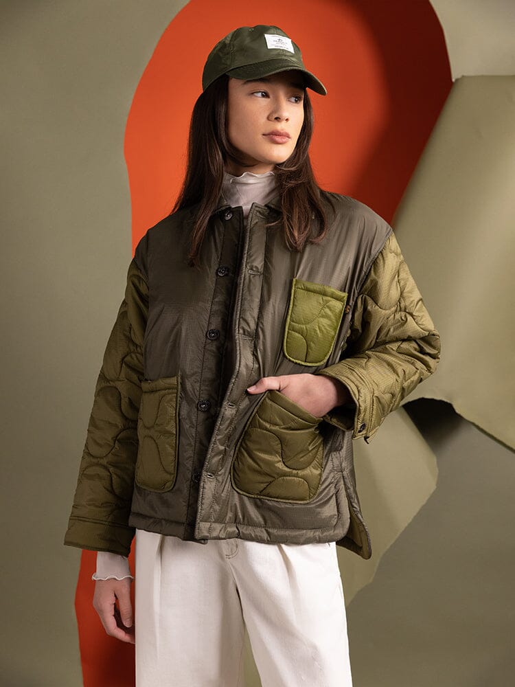 A person wearing the Women's Insulated Chore Coat by Alpha Industries in olive green, complemented with white pants and a matching cap.