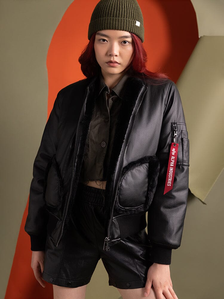 A person wearing an the Women's Reversible Faux Leather MA-1 Bomber Jacket in black by Alpha Industries.