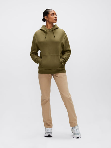 A person wearing the Alpha Hoodie by Alpha Industries, Inc., featuring a green unisex design with Alpha applique, pairs it with beige pants, highlighting the comfort of cotton fabric.