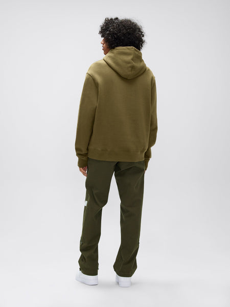 A person in a green unisex Alpha Hoodie and matching pants, showcasing an Alpha applique, stands with their back to the camera. Designed by Alpha Industries, Inc., this outfit is crafted from comfortable cotton fabric and perfectly blends style with simplicity.