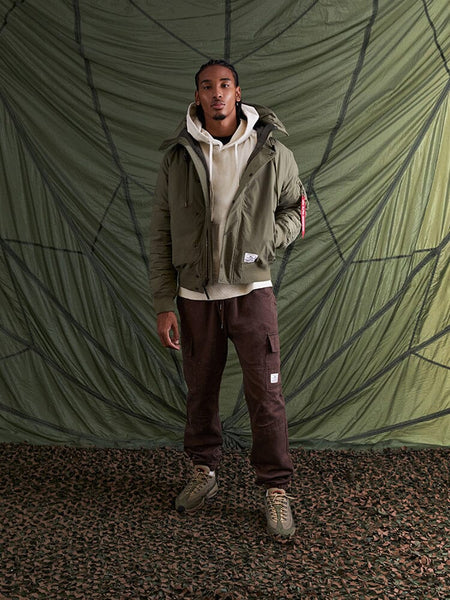 A person stands wearing the olive green Alpha Industries N-2B Altitude Parka.