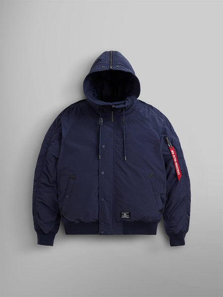 N-2B Altitude Parka, in blue, by Alpha Industries features an adjustable split hood and a red tag on the sleeve. This water-resistant bomber jacket comes with snap buttons and a front zipper closure.