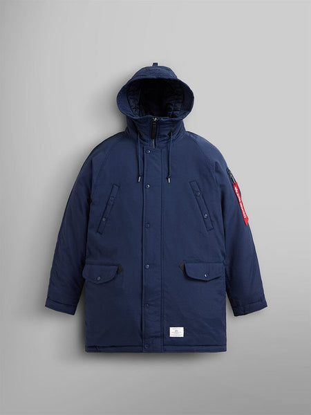 The N-3B Altitude Mod Parka by Alpha Industries, in a replica blue color, showcases a buttoned front, two large pockets, and a striking red zipper tag on the left sleeve.